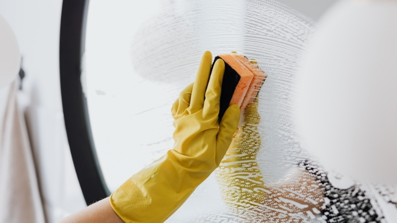 Cleaning bathroom mirror and tiles with rubber gloves